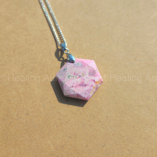 Hexagonal pink stone pendant on a chain against a beige background
