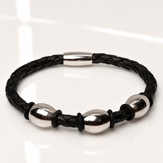 A black braided leather bracelet with three polished silver steel oval beads and a matching silver clasp, displayed on a clean white reflective surface.