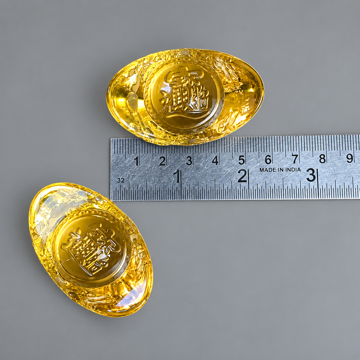 Two gold-colored oval pendant charms with embossed Chinese characters, displayed on a gray background with a metal ruler for scale.