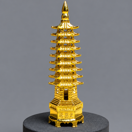 A miniature golden pagoda sculpture displayed on a round black base against a solid gray background.