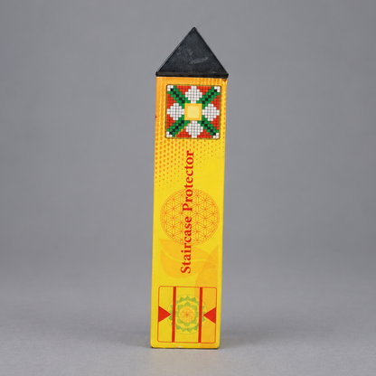 A yellow rectangular staircase protector with a black pointed top, standing upright against a neutral gray background. The box features a colorful geometric pattern near the top and red text reading 'Staircase Protector'.