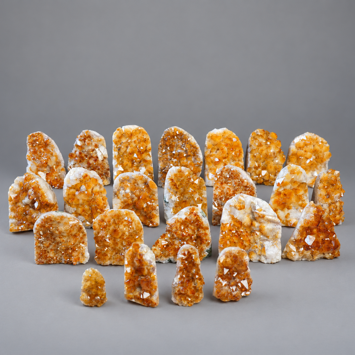 A collection of natural citrine crystal clusters and geode pieces arranged on a neutral gray studio background.