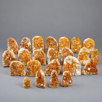 A collection of natural citrine crystal clusters and geode pieces arranged on a neutral gray studio background.