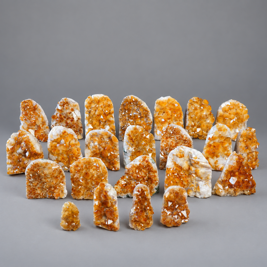 A collection of natural citrine crystal clusters and geode pieces arranged on a neutral gray studio background.