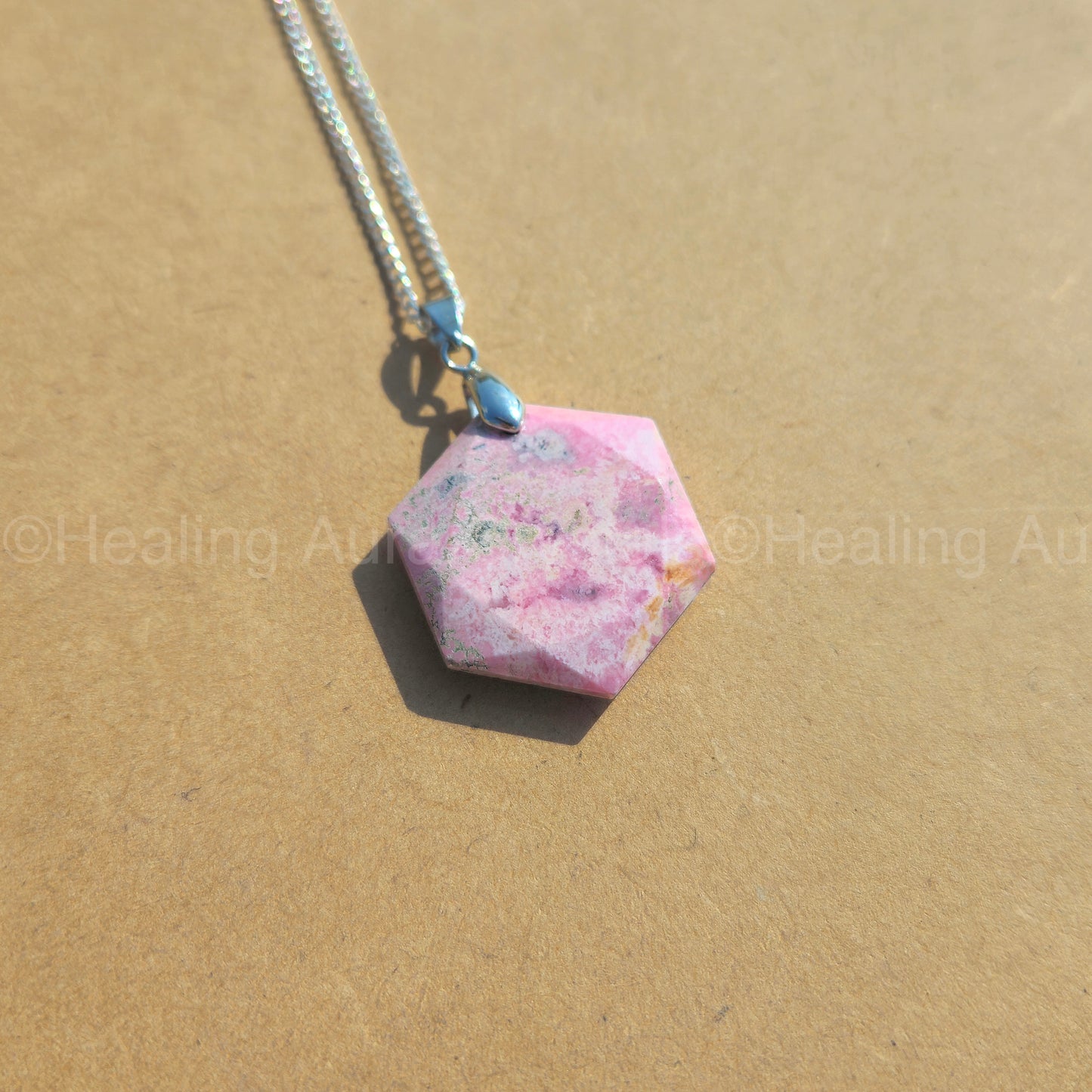 Hexagonal pink stone pendant on a chain against a beige background