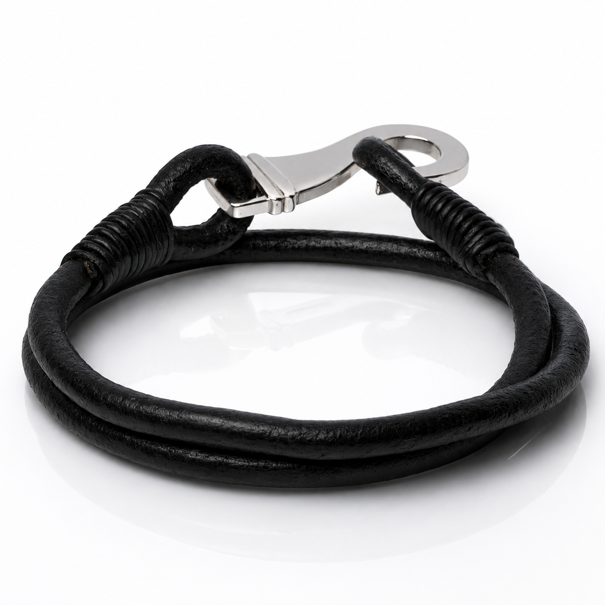 A black leather bracelet with a silver-toned lobster clasp, coiled on a reflective white surface.