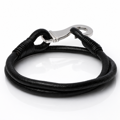 A black leather bracelet with a silver-toned lobster clasp, coiled on a reflective white surface.