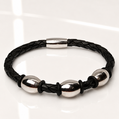 A black braided leather bracelet with three polished silver steel oval beads and a matching silver clasp, displayed on a clean white reflective surface.
