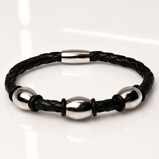 A black braided leather bracelet with polished silver steel beads and a silver clasp, displayed on a clean white reflective surface.