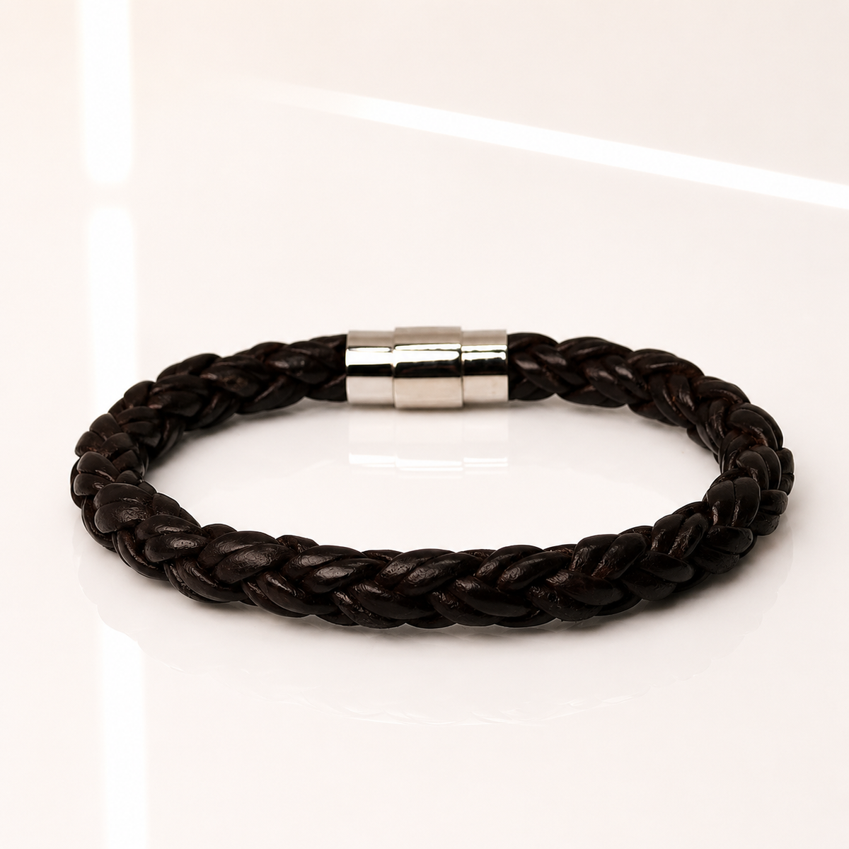 A dark brown braided leather bracelet with a polished silver magnetic clasp, displayed on a clean white reflective surface.