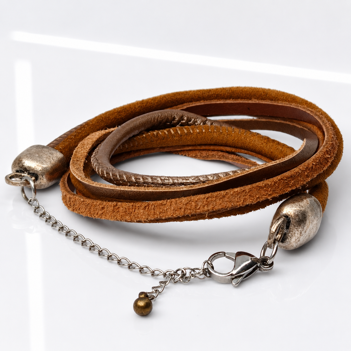 A multi-strand wrap bracelet featuring brown suede and leather bands, accented with antique silver-tone metal end caps, a short chain link, and a small dangling bead.