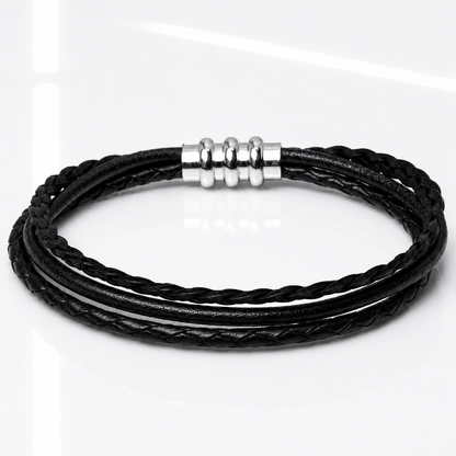 A black multi-strand braided leather bracelet with a polished silver-toned metal clasp, displayed on a clean white reflective surface.